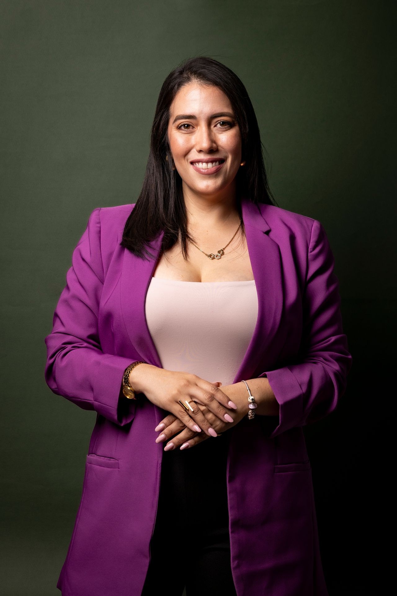 Woman in a purple blazer smiling, standing against a dark green background.