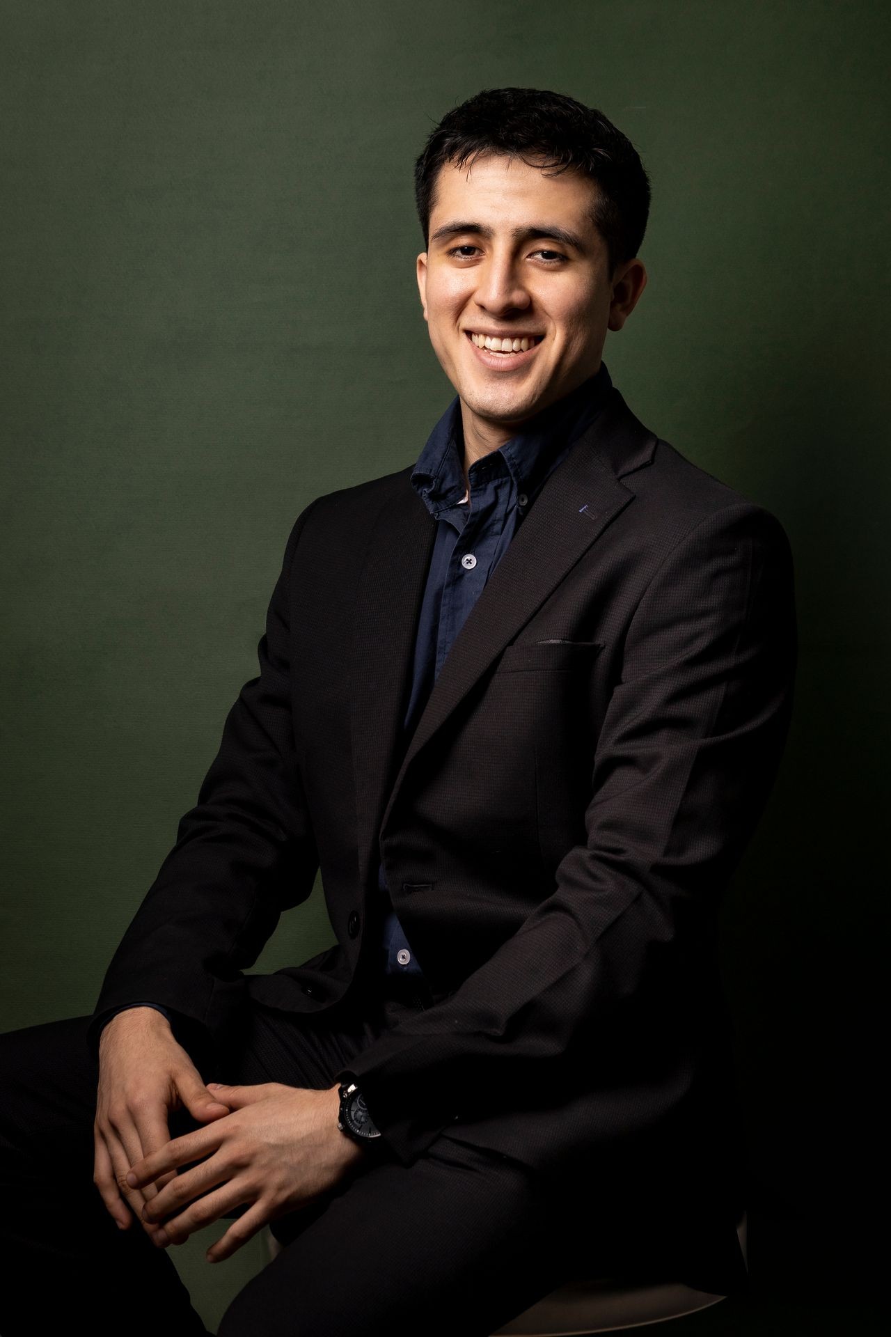 Smiling person in a dark suit sitting against a green background.