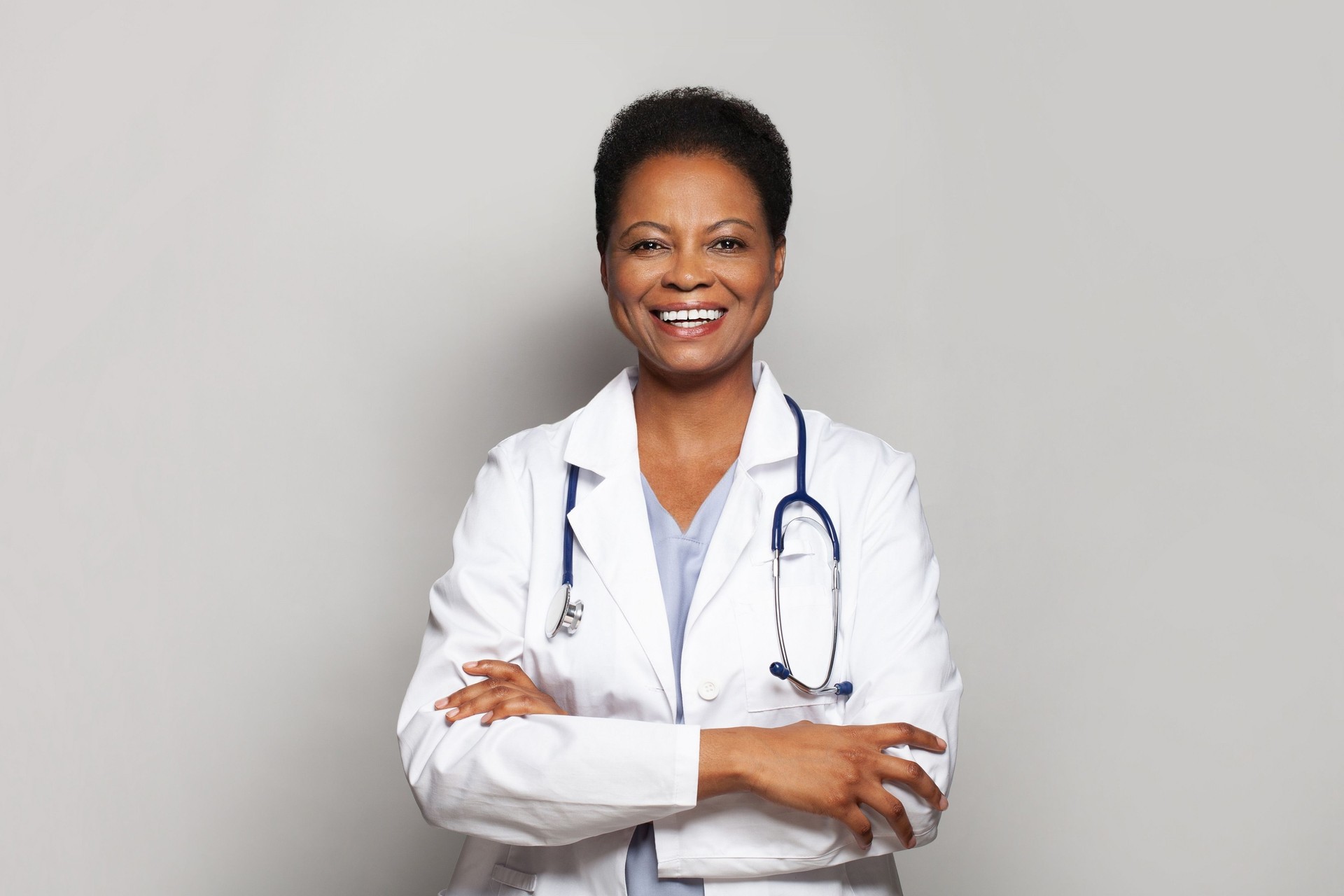 Feliz trabajadora médica exitosa de la doctora en bata blanca de laboratorio de pie con los brazos cruzados sobre fondo blanco